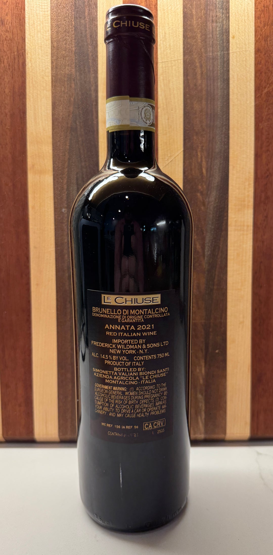 A bottle of Le Chiuse Annata 2021 Red Wine, showing the back label, set against a wooden striped background.